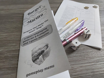 a photo of a folded paper gameplay menu tilted "burger maestro - a short roleplaying game for 2-6 players"